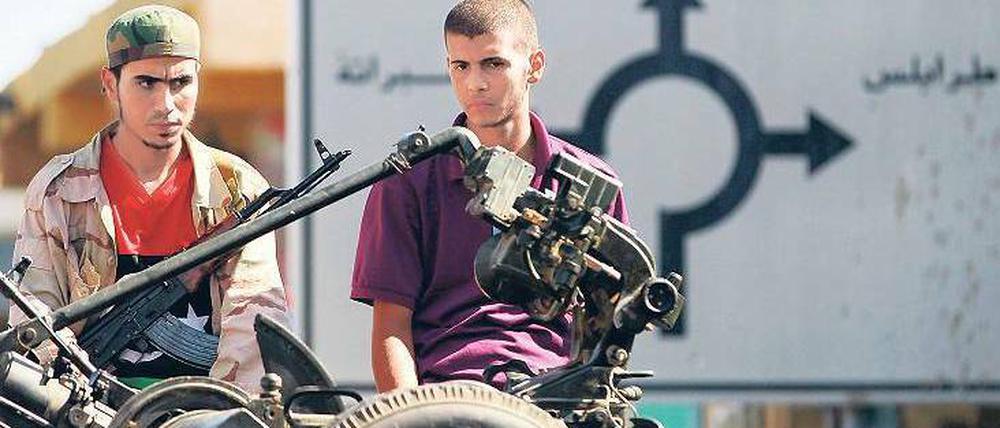 Wo geht es zur Hauptstadt? Rebellen in der angeblich fast vollständig eroberten Küstenstadt Al Sawija vor einem Kreuzungsschild, das den Weg nach Tripolis anzeigt. Foto: Reuters