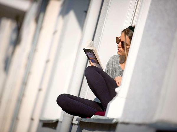Eine junge Frau sitzt mit einem Buch am Fenster.