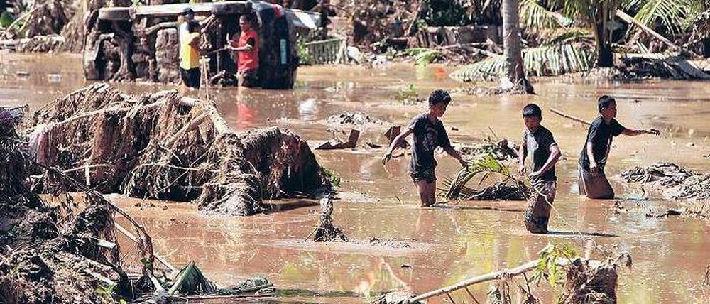 Katastrophengebiet Mindanao. Bewohner waten durch den Schlamm, den die Sturzflut hinterlassen hat. Fotos: dpa(2)