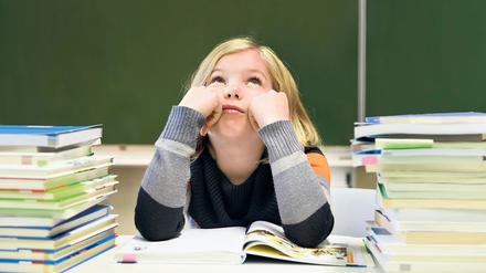 Schülerin, 9 Jahre, gelangweilt, mit zwei Stapeln Bücher vor einer Tafel.