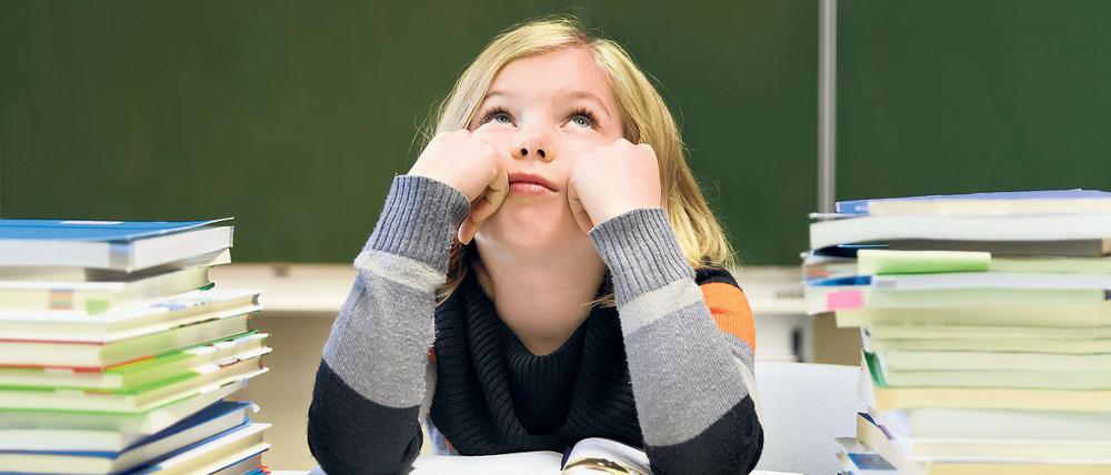 Schülerin, 9 Jahre, gelangweilt, mit zwei Stapeln Bücher vor einer Tafel.