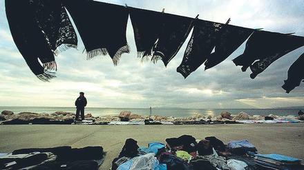 Am Minimum. Ein chinesischer Einwanderer verkauft an einem Strand vor Athen Kleider. 