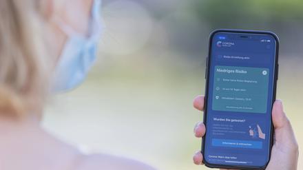 Eine junge Frau mit Mund-Nasen-Schutz benutzt die Corona-Warn-App auf ihrem Smartphone.