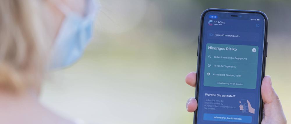 Eine junge Frau mit Mund-Nasen-Schutz benutzt die Corona-Warn-App auf ihrem Smartphone.
