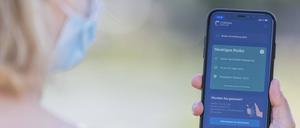 Eine junge Frau mit Mund-Nasen-Schutz benutzt die Corona-Warn-App auf ihrem Smartphone.