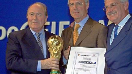 Lächeln süßsauer. Joseph Blatter überreicht Deutschlands Bewerbungschefs Franz Beckenbauer und Fedor Radmann den WM-Pokal. Blatters Favorit für 2006 war Südafrika.