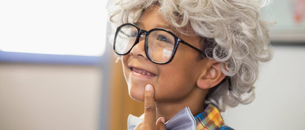 Thoughtful schoolboy wearing wig in classroom.