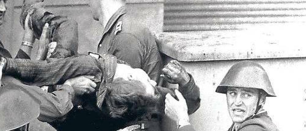 Ein Foto für den Geschichtsunterricht: Eines der bekanntesten Maueropfer, Peter Fechter, wird nach seinem missglückten Fluchtversuch und einer Ewigkeit, die er in seinem Blut lag, von einem Grenztrupp aus dem Todesstreifen geholt. Zu diesem Zeitpunkt lebte er noch. Links: Hauptmann Schäfer und Oberfeldwebel Wurzel (unten); rechts: Volkspolizeiobermeister Mularczyk, darunter Gefreiter Lindenlaub.