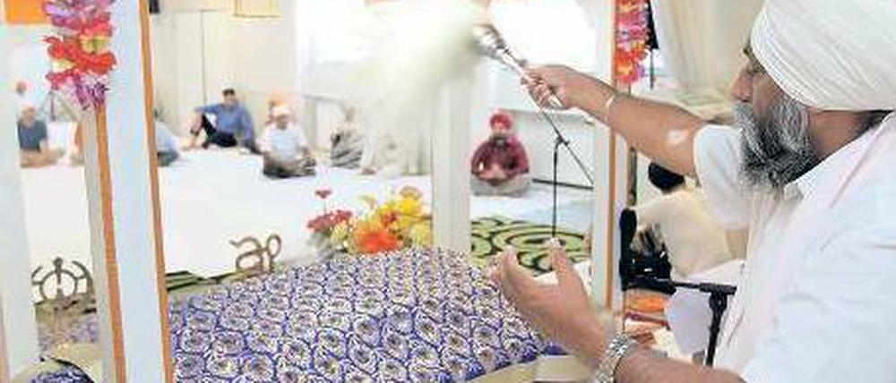 Gut gefächelt. Das heilige Buch der Sikh liegt während des Gottesdienstes im Reinickendorfer Tempel auf einem Bett. Ein Gemeindemitglied fächelt ihm Luft zu. Foto: Davids/Darmer