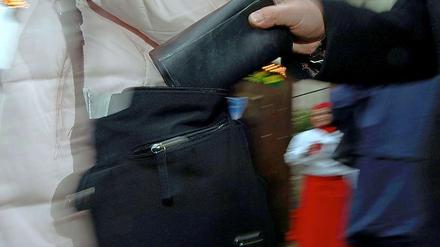 Ein Taschendieb zieht eine Geldbörse aus einer Handtasche.