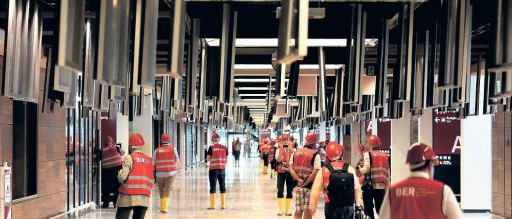 Während der Ila wurden Reporter über die Baustelle geführt. Im BER-Terminal sind die Deckenklappen geöffnet; darunter wird an den Kabeltrassen gearbeitet. Die Geräte und Sitzbänke sind mit Schutzfolie geschützt.