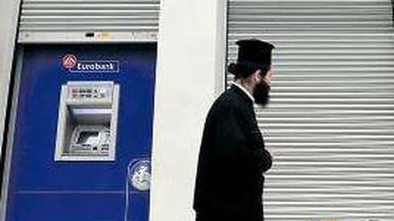 Knapp bei Kasse. Ein griechisch-orthodoxer Priester geht an einer Bankfiliale vorbei, die wegen eines Streiks der Angestellten geschlossen ist.