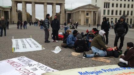 Auf Pappunterlagen und ihren Rucksäcken sitzen die Flüchtlinge am Brandenburger Tor.