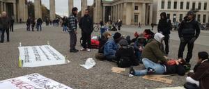 Auf Pappunterlagen und ihren Rucksäcken sitzen die Flüchtlinge am Brandenburger Tor.