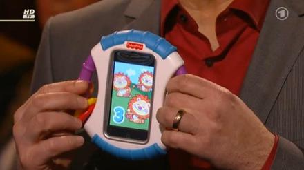 Frank Plasberg hält in seiner Sendung "Hart aber fair" eine iPhone-Rassel für Babys in die Kamera.