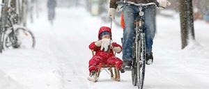 Ein Radler zieht sein Kind auf dem Schlitten. 