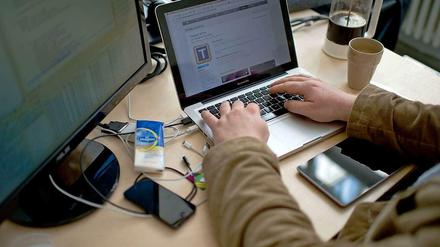 Mann arbeitet am Laptop. Daneben ein Bildschirm, ein Smartphone, ein Tablet. 