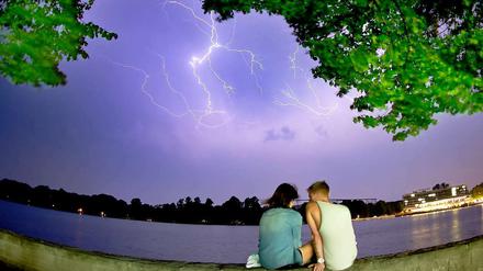 Ein junges Paar sitzt am späten Mittwochabend am Maschsee in Hannover (Niedersachsen), als am Himmel Blitze von einem aufziehenden Gewitter zu sehen sind.