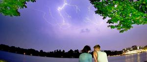 Ein junges Paar sitzt am späten Mittwochabend am Maschsee in Hannover (Niedersachsen), als am Himmel Blitze von einem aufziehenden Gewitter zu sehen sind.