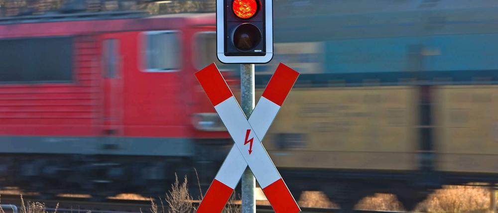 Ein Güterzug passiert einen Bahnübergang, das Signal für den Autoverkehr steht auf Rot. 