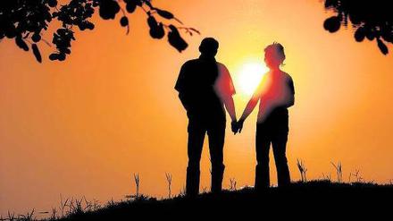 Ein Mann und eine Frau stehen Hand in Hand vor einem Sonnenuntergang.