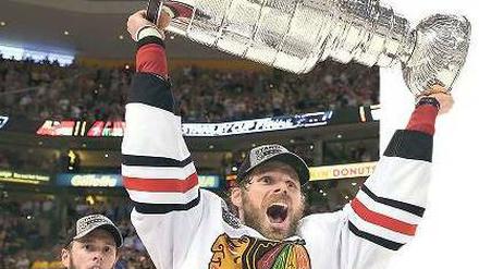 Potthässlich, aber sehr begeht. Chicagos Michal Handzus stemmt den schweren Stanley Cup in die Höhe, nachdem er ihn von Kapitän Jonathan Toews (l.) bekommen hat. Foto: AFP