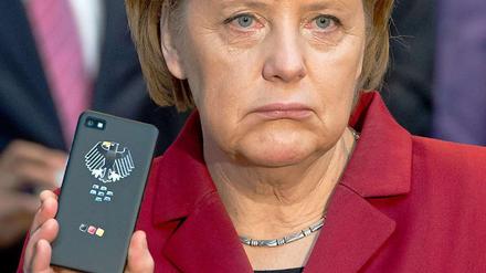 Angela Merkel zeigt auf der Cebit die Rückseite eines Smartphones, auf dem ein Bundesadler zu sehen ist.