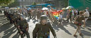 Polizisten in Kampfkleidung als Spalier neben ein paar hundert Demonstranten mit Regenbogenfahne