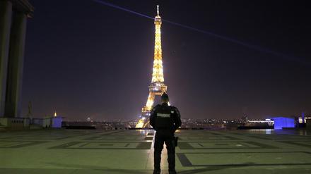 Ein Polizist patrouilliert am Trocadero vor dem beleuchteten Eiffelturm in Paris (Frankreich).
