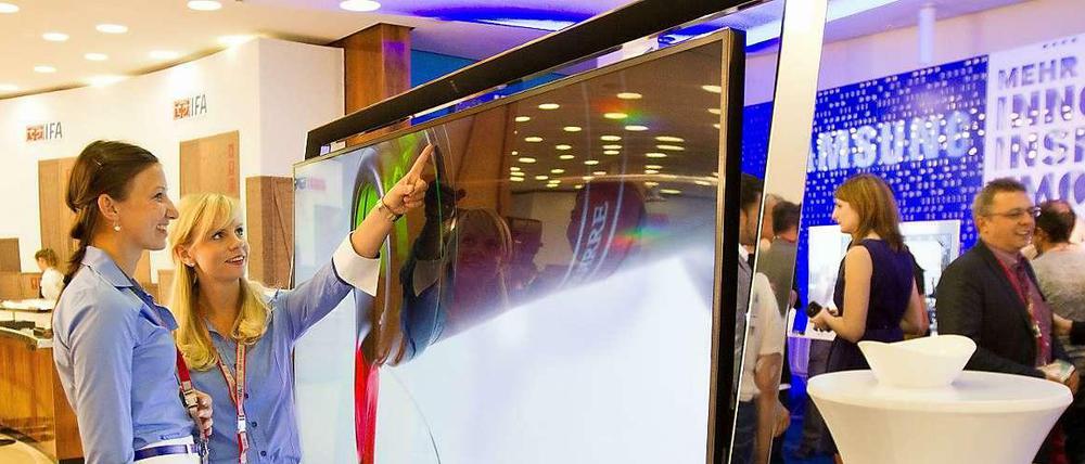 Die beiden Frauen stehen vor einem flachen Fernseher, der in einem Metallrahmen hängt. Das Gerät ist mit Rahmen mehr als zwei Meter hoch und 1,60 Meter breit.