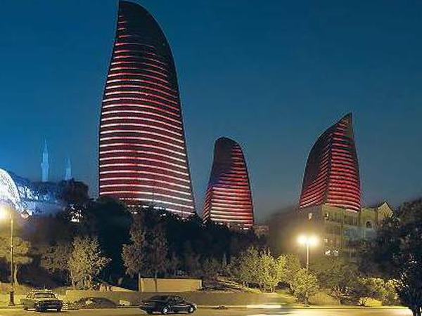 Die Form der Flame Towers in Baku erinnert an Flammen. Die Hochhäuser leuchten rot vor dem dunklen Himmel, die Fensterreihen bilden erleuchtete Streifen. 