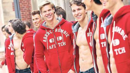 Junge männlichen Models tragen rote Jacken mit der Aufschrift Abercrombie & Fitch. Einige tragen die Jacken offen, so dass die muskulösen Bäuche zu sehen sind.