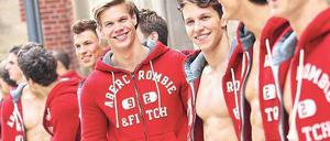 Junge männlichen Models tragen rote Jacken mit der Aufschrift Abercrombie & Fitch. Einige tragen die Jacken offen, so dass die muskulösen Bäuche zu sehen sind.