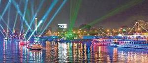 Bunte Schiffe auf dem glitzernden Wasser, bunte Scheinwerfer, die in den nächtlichen Himmel strahlen, hinten sieht man den Fernsehturm.
