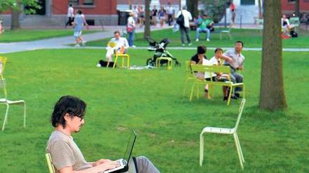 Ein Student sitzt mit seinem Laptop auf dem Rasen vor der Uni.