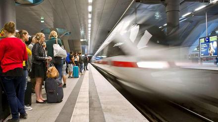Ein ICE fährt in einen Bahnhof ein, auf dem Bahnsteig warten viele Reisende.