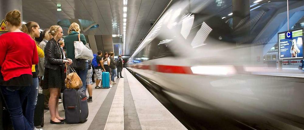 Ein ICE fährt in einen Bahnhof ein, auf dem Bahnsteig warten viele Reisende.