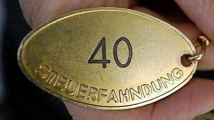Eine metallene Marke mit der Aufschrift "Steuerfahndung" und der Zahl 40 wird von einem Menschen festgehalten.
