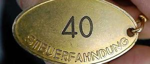 Eine metallene Marke mit der Aufschrift "Steuerfahndung" und der Zahl 40 wird von einem Menschen festgehalten.