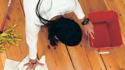 Eine Frau kniet auf einem Dielenboden und putzt