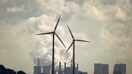 Vor einem herkömmlichen Kraftwerk mit großen Kühltürmen drehen sich vier Windräder.