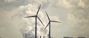 Vor einem herkömmlichen Kraftwerk mit großen Kühltürmen drehen sich vier Windräder.