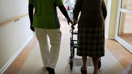 Beine einer Pflegerin und einer alten Frau mit Rollator von hinten auf einem langen Flur