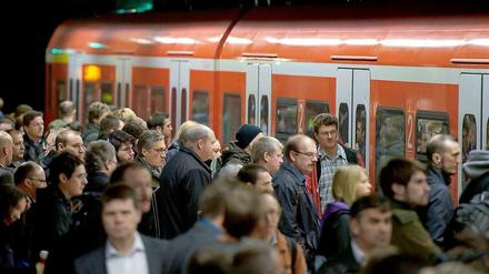 Reisende drängeln sich an einem Nahverkehrszug der Bahn. 