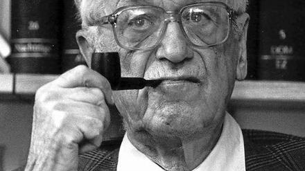 Theodor Eschenburg sitzt Pfeife rauchend vor einer Bücherwand.