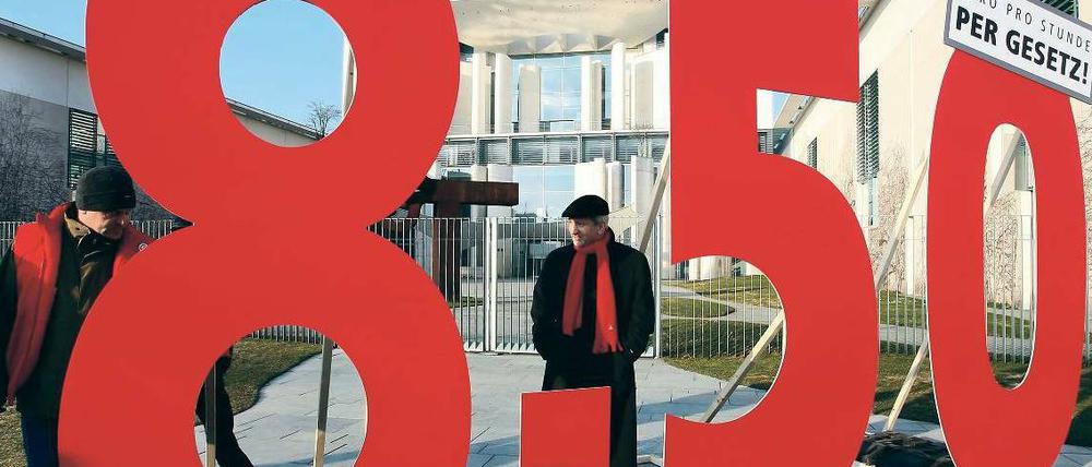 Vor dem Kanzleramt in Berlin bilden übermannshohe Ziffern den Betrag 8,50; zwei Männer betrachten diese.