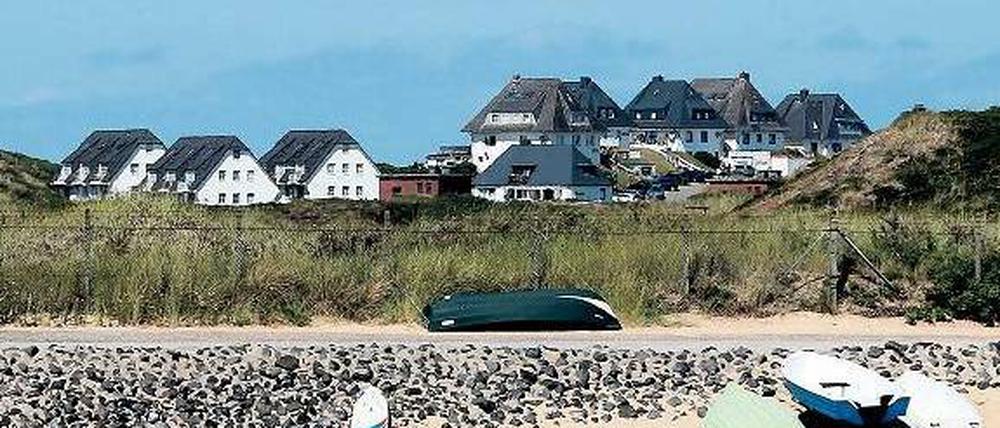 Hinter Dünen stehen einige Mehrfamilienhäuser. 