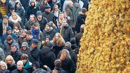 Viele Menschen drängeln sich in einer Einkaufsstraße an einem goldenen Kunstweihnachtsbaum vorbei