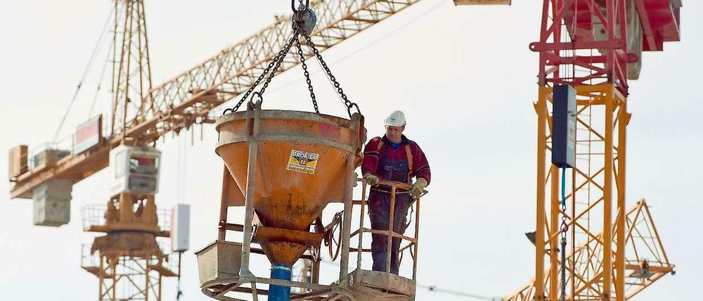 Ein Bauarbeiter lässt sich auf einer Betonpumpe stehend von einem Kran in die Höhe ziehen.