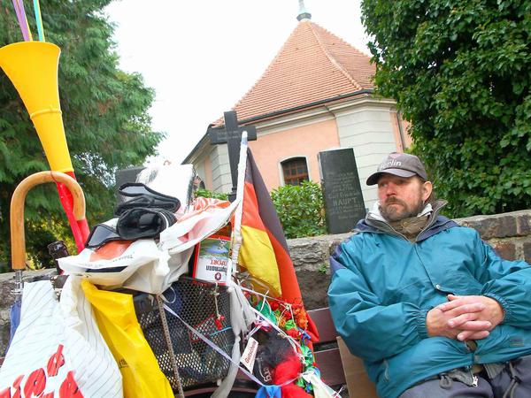 Sein Platz, vor dem Friedhof an der alten Dorfkirche. Auf seinem Fahrrad hängt sein Hab und Gut und ein bisschen etwas zur Zierde.
